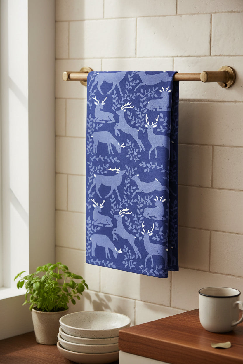 A rectangular tea towel featuring a repeating pattern of deer and leafy branches in shades of blue and white, in a country kitchen