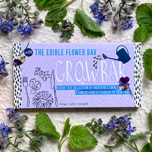 Edible flower bar packaging surrounded by various edible flowers on a textured surface