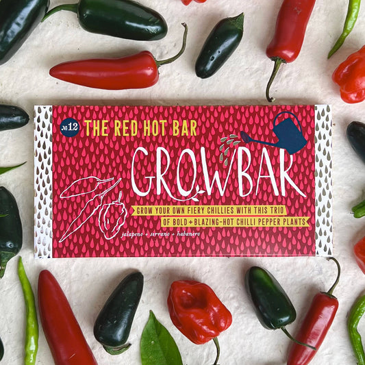 A packaged hot chili pepper blend bar by The Red Hot Bar, labeled 'Crowbar' (12), styled in a flat-lay with fresh red and green chili peppers and green leaves on a textured off-white background.